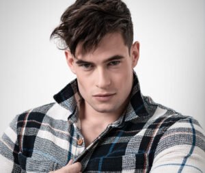 Callboy Salzburg looks seductively into the camera and holds his shirt with one hand